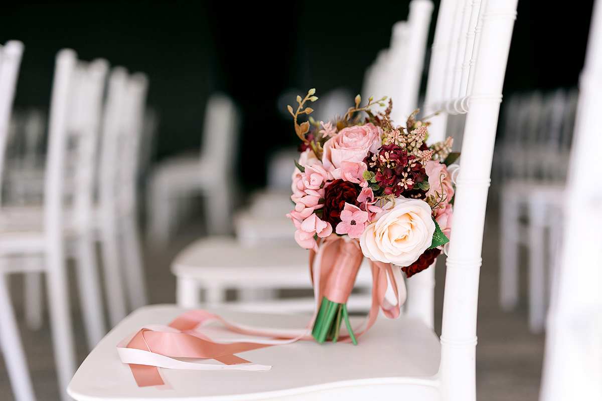 Romantic wedding bouquet with pink and burgundy flowers and satin ribbons, styled on a white ceremony chair at a Brisbane Registry wedding.