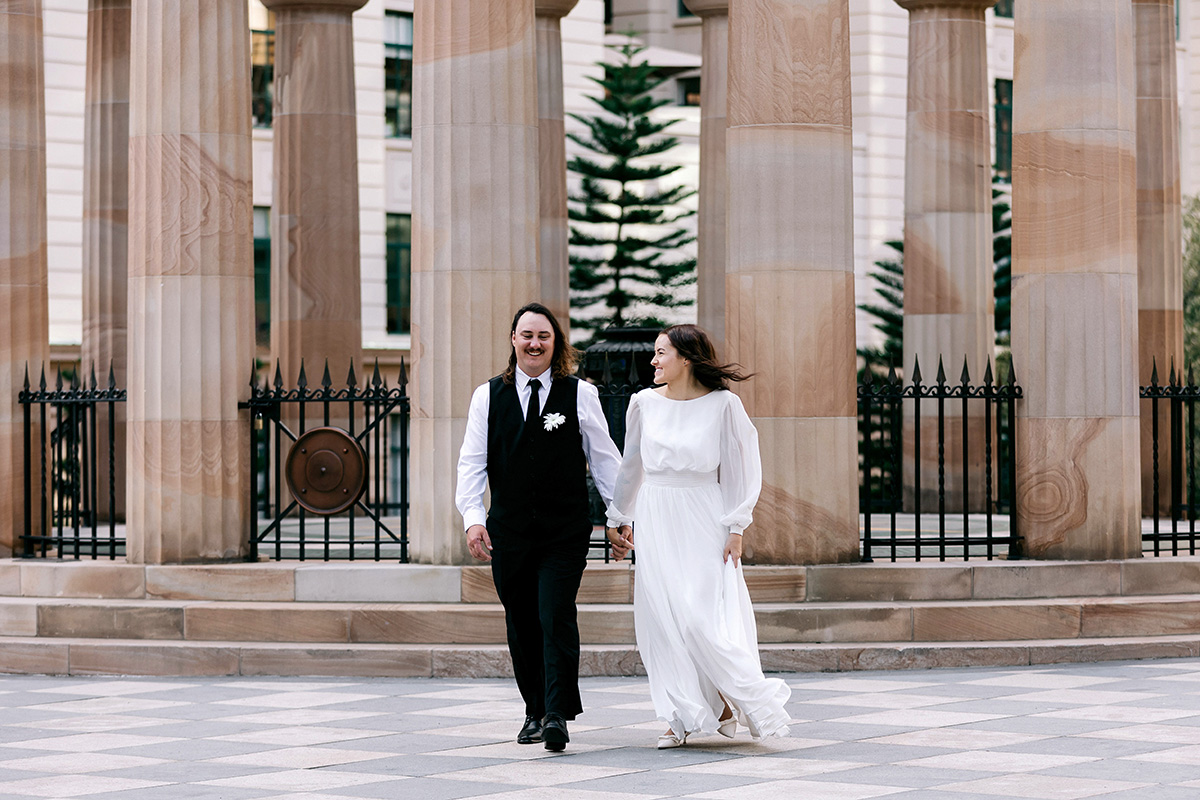 Just married couple walking hand in hand in front of sandstone pillars at Anzac Square Brisbane
